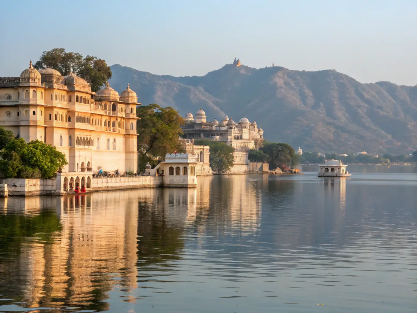 A serene image of a boat ride on Lake Pichola at sunset, with the City Palace and Jag Mandir in the background, capturing the romantic ambiance of Udaipur.